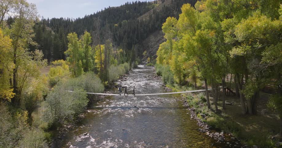 Three hikers cross the bridge over the stream