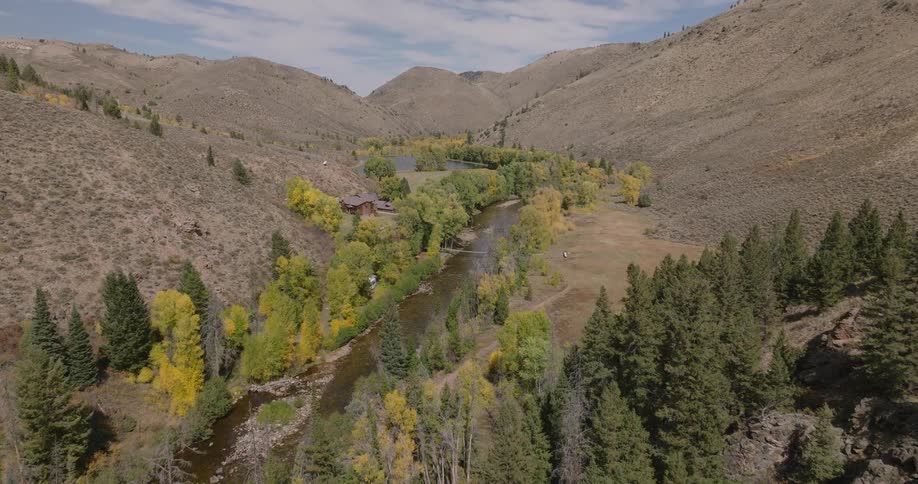An aerial view shows a river winding through a valley with hills on both sides surrounded by green and yellow trees