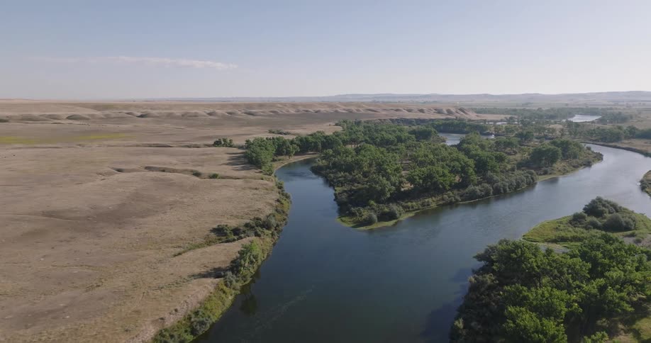 A winding river flows through a grassy plain with patches of dense trees on its banks