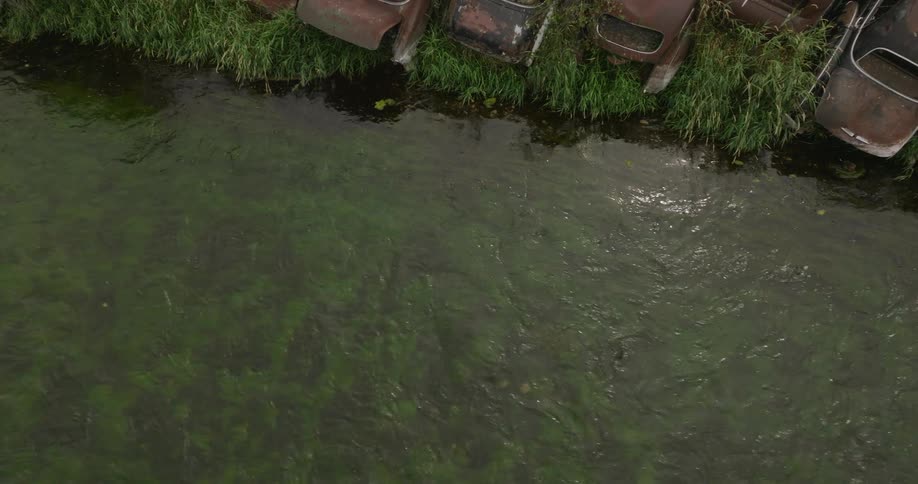 Rusted broken down vehicles are on the side of the stream