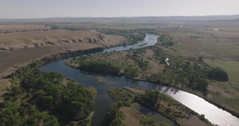 A winding river flows through a dry hilly landscape with scattered trees and farmland