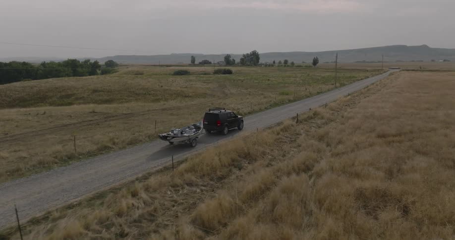 Aerial of a vehicle towing a boat on a road in the middle of a rural area during daytime