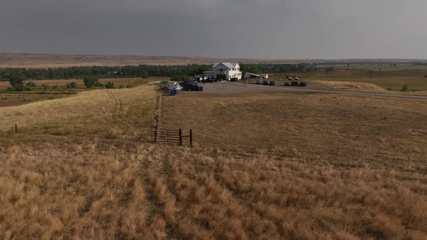 Rows of boats connected to trucks are parked by the farm house