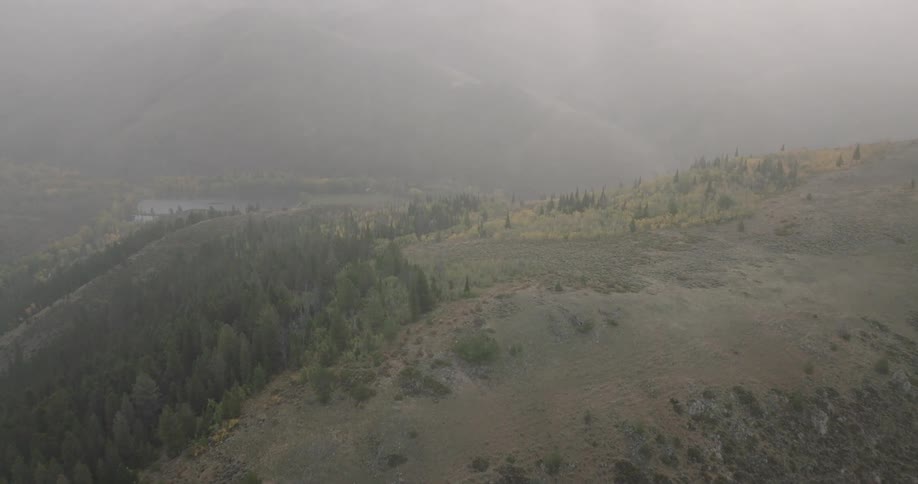 A hazy aerial view of a mountain landscape with forested slopes and a distant lake