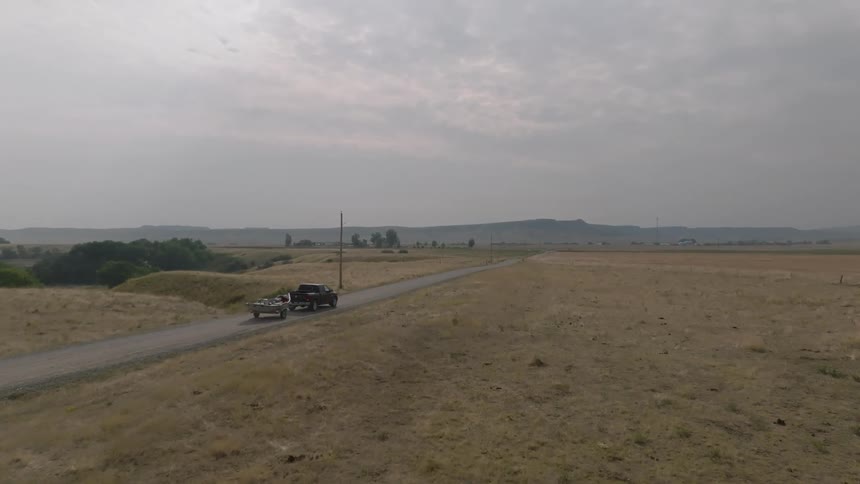 A truck towing a boat is driving on a rural road