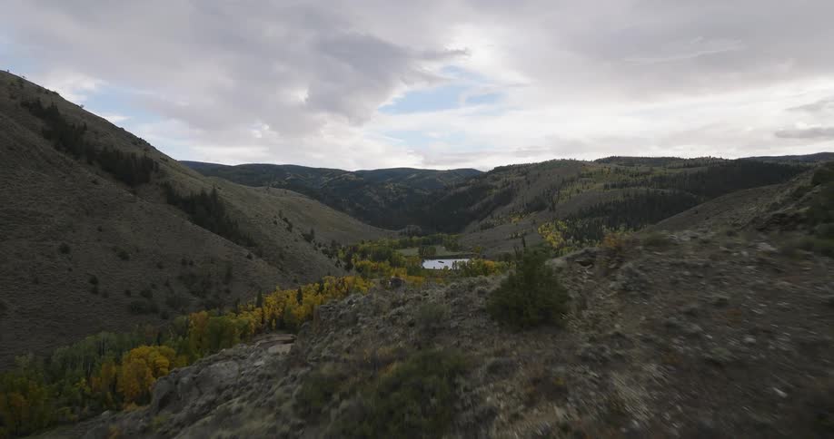 An aerial view flies forward over a vast mountain valley descending towards a winding river surrounded by colorful autumn trees