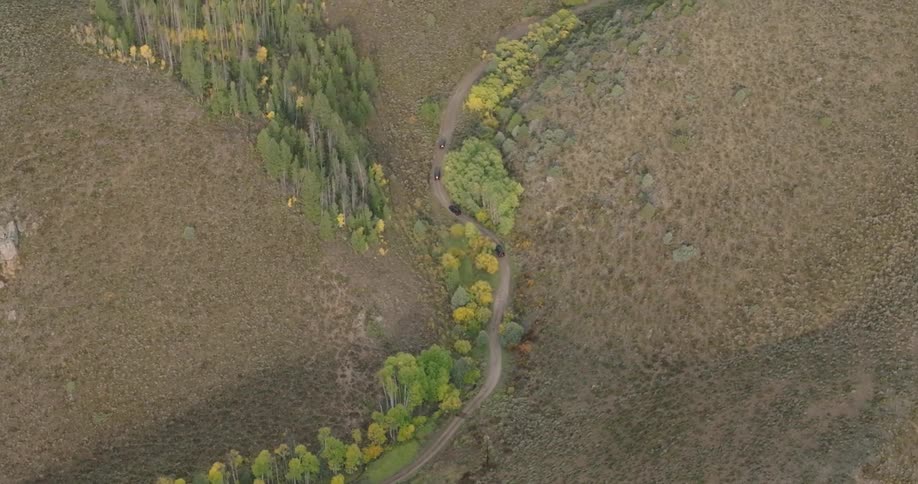 Vehicles drive along a highway winding past hills and groves of trees on an autumn day