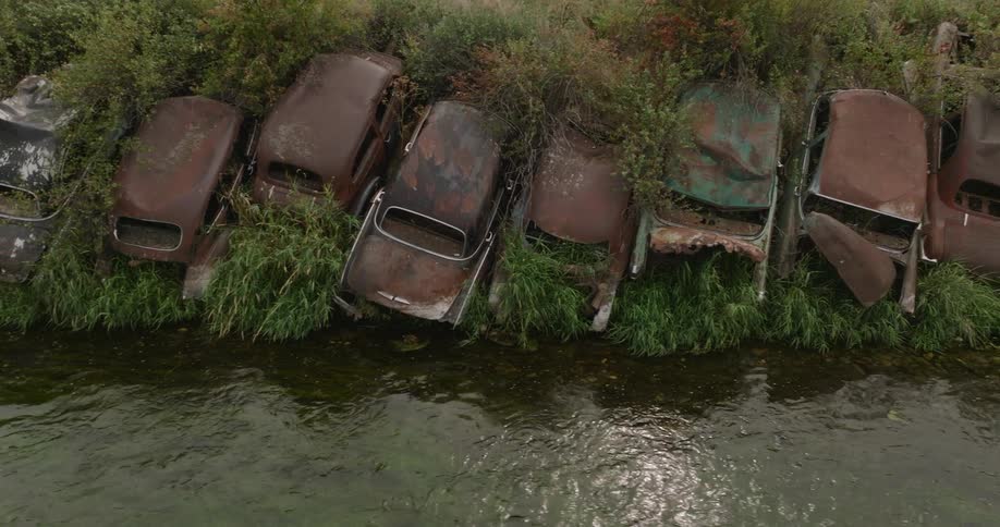 Rusted out old cars are on the hill by the moving stream