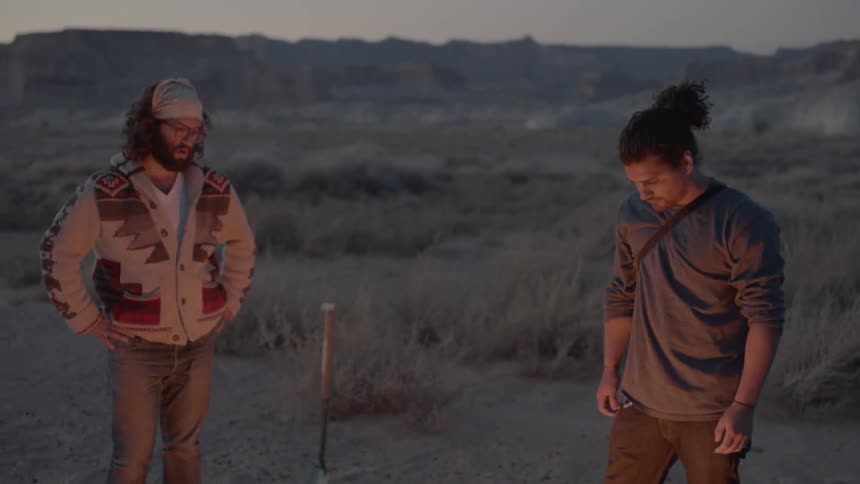 Two men stand near a fire