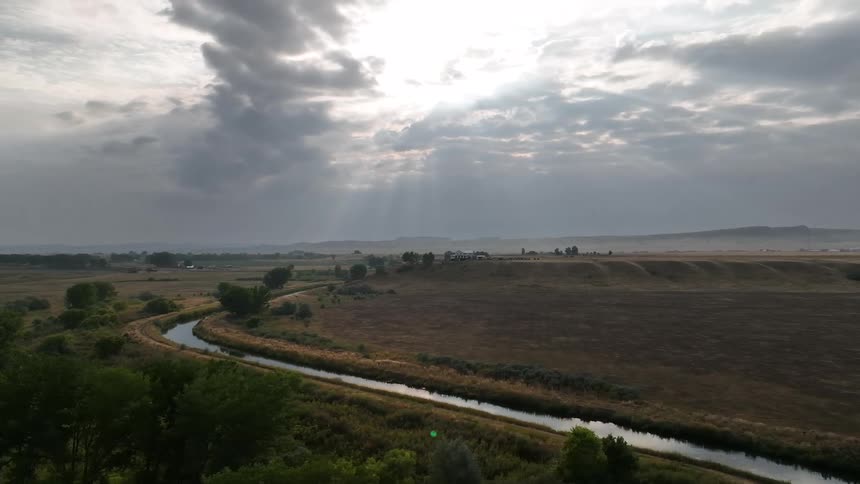 A winding river runs through an open landscape under dramatic cloudy skies