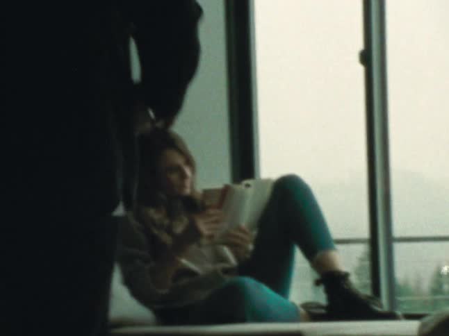 A man takes a coffee from the table and gives it to a woman sitting on the couch by the window reading