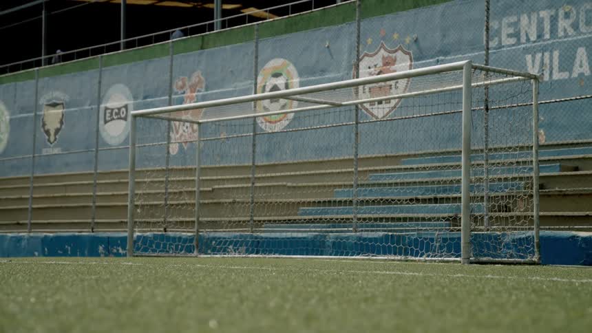 An empty metal soccer goal stands on a turf field beside vacant bleachers
