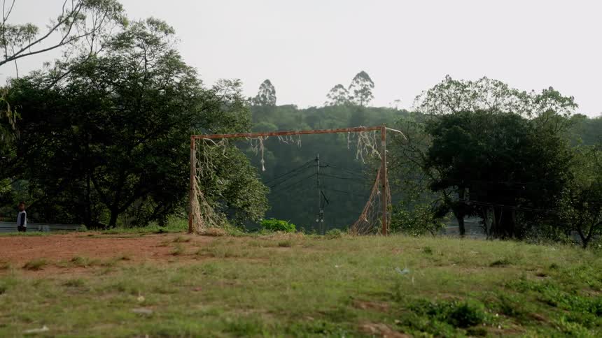 Two children hanging out near an old soccer goal whose net has been torn away