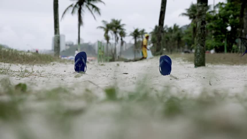Bottom half of black flip flops buried in the sand at a beach