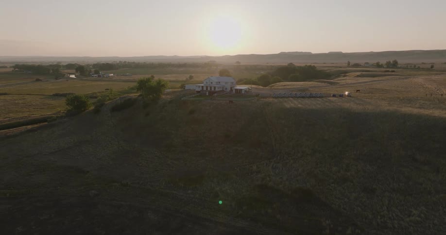 An aerial view shows a white building on a hill with a winding river and lush landscape in the background under a hazy sky