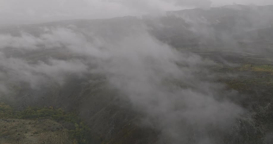 An aerial shot shows a flight through thick clouds and fog gradually revealing a vast mountainside landscape