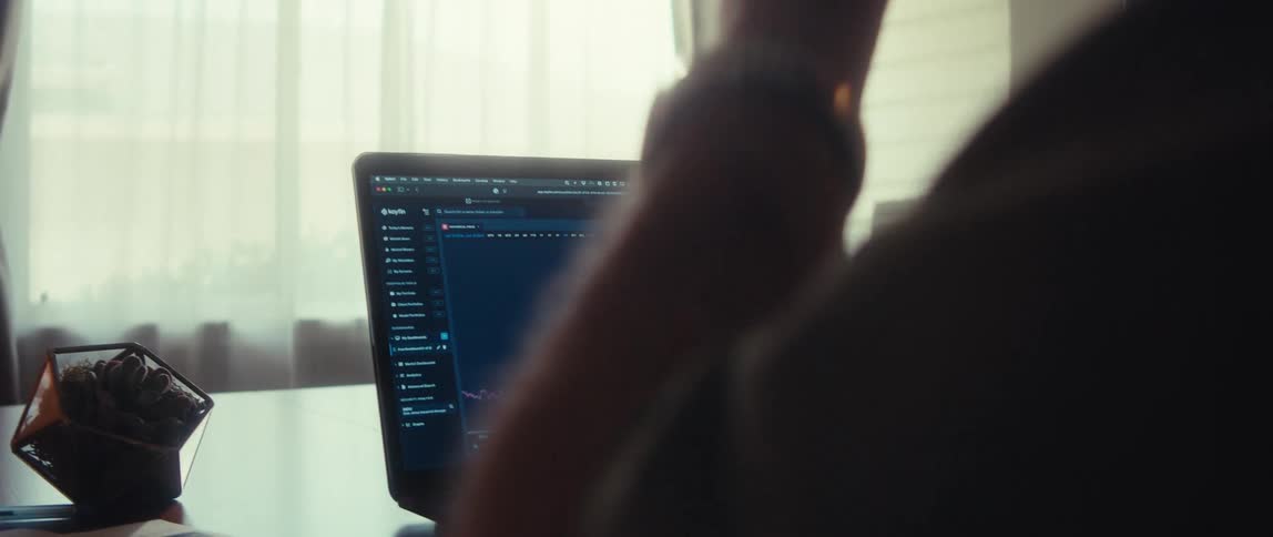 A person is holding glasses while looking at a laptop screen that has some green and red line graphs