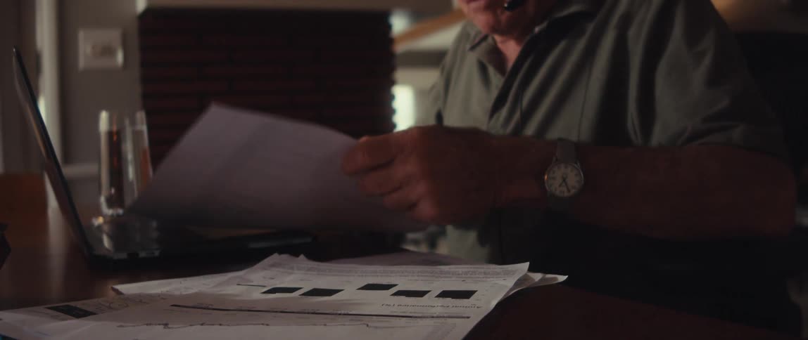 Elderly man wearing a headset holds and examines several white papers filled with charts and text