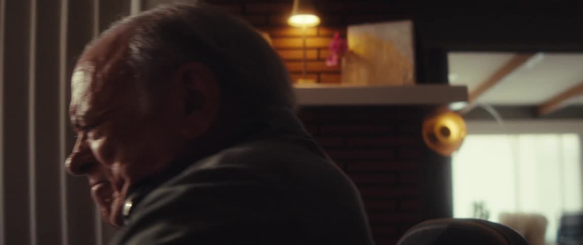 An elderly man sitting in his living room shifts from sadness to fury and anger