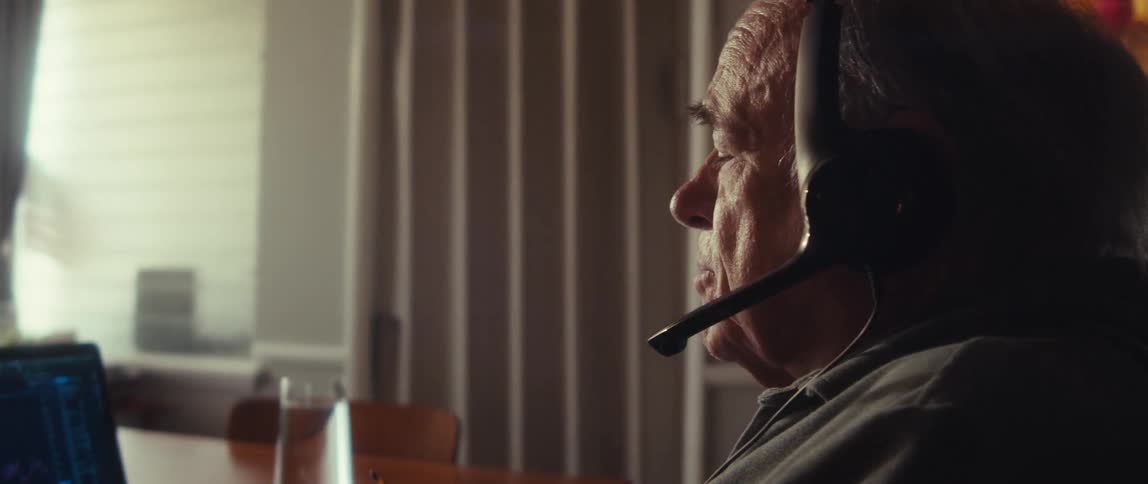 Elderly man sitting with headphones and facing a laptop