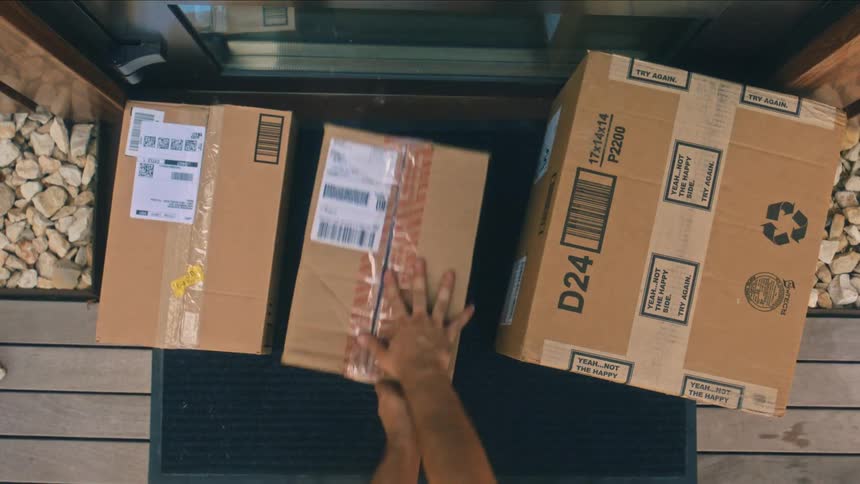 A person drops various delivery boxes at a doorstep during daytime