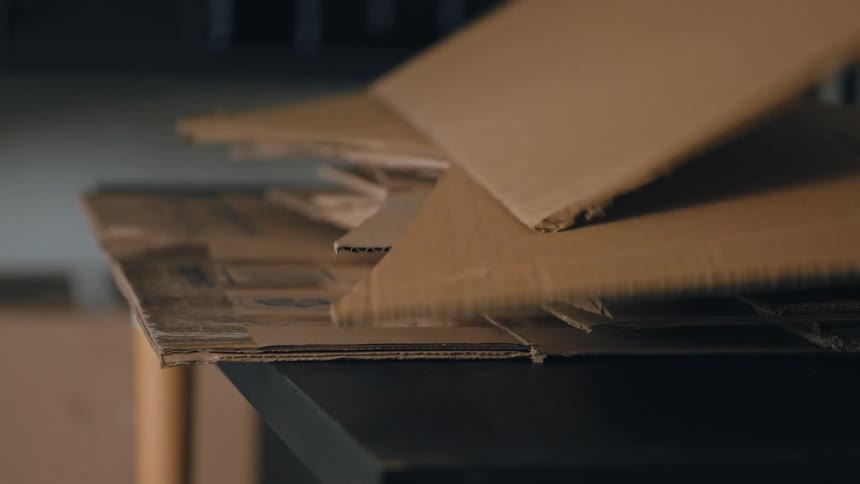 In a fastpaced timelapse a hand quickly stacks a large growing pile of flattened cardboard boxes onto a black table in a stockroom