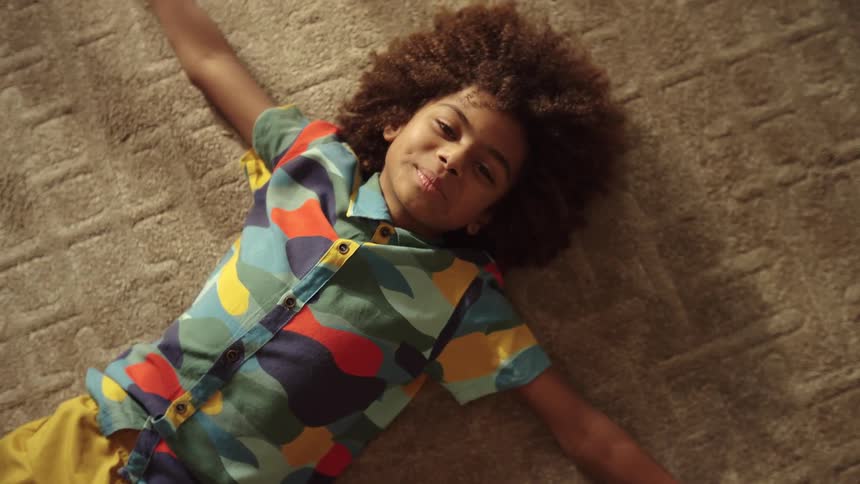 The face of a little boy who is smiling and lying on the floor on a carpet and with his arms open