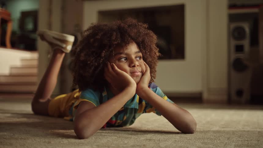 A smiling child lies on the floor with hands on cheeks looking happy and relaxed
