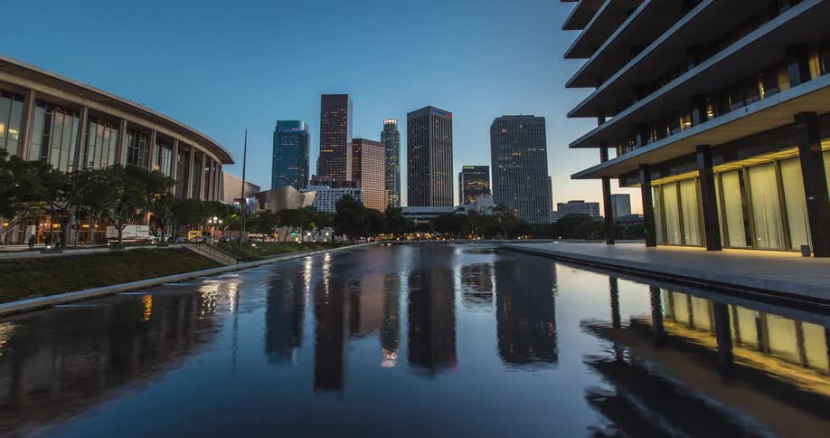 A modern cityscape of Los Angeles with tall buildings reflected in a calm urban pool at sunset