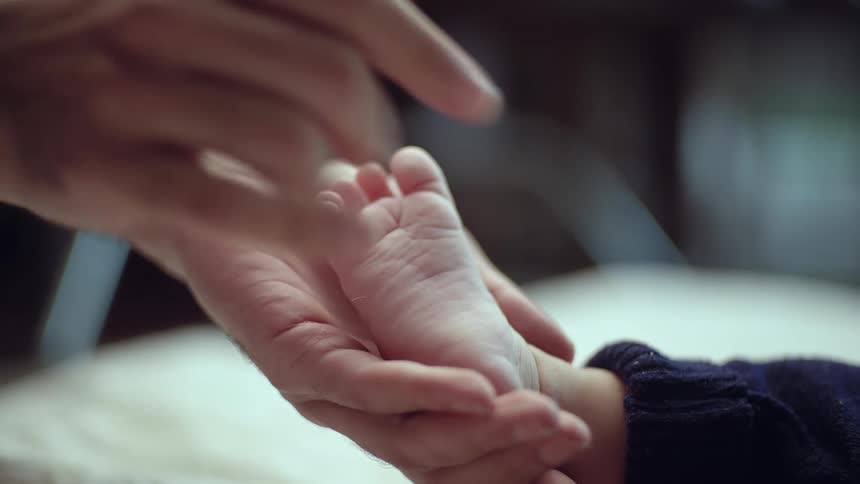 Close up a mother gently rubbing the sole of her babys feet with her palm