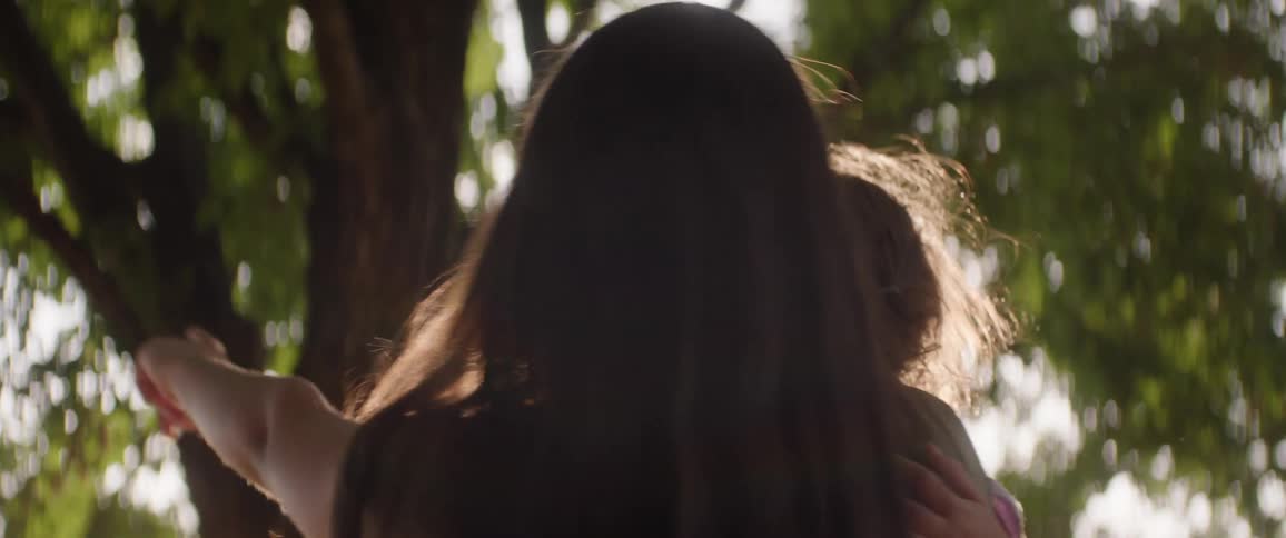 The sun shines through the tree on the teenager holding her sister