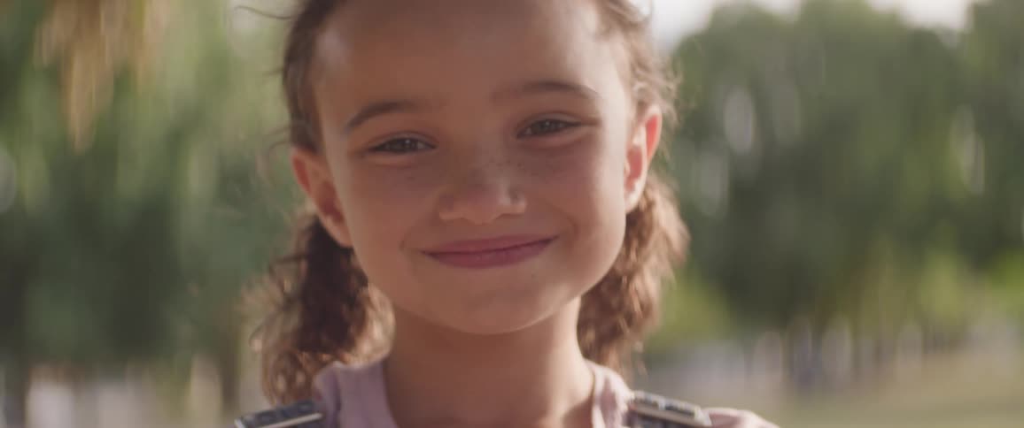 A young girl stands in the park with a smile on her face at midday