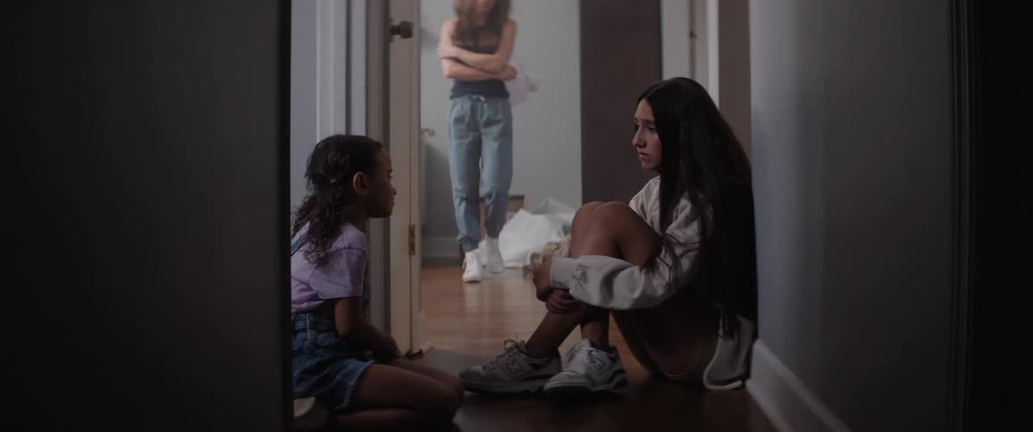 Two girls sit on the floor while a woman paces the floors next to them