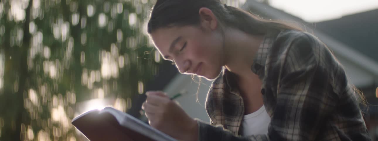 Teenage girl smiles while drawing in a sketchbook