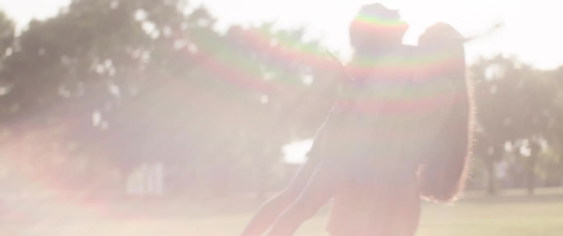 A teenage girl plays with a child carrying her and spinning around in a 360degree turn while in the park on a sunny day