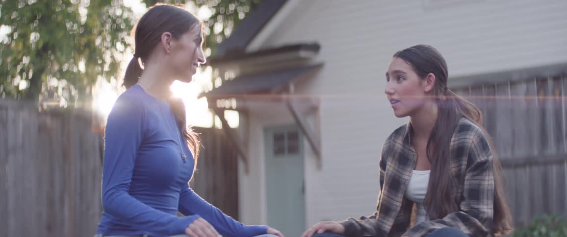 Two girls are sitting on the grass talking