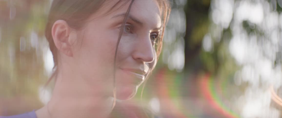 A young woman stands out in the open on a sunny day with a smile on her face