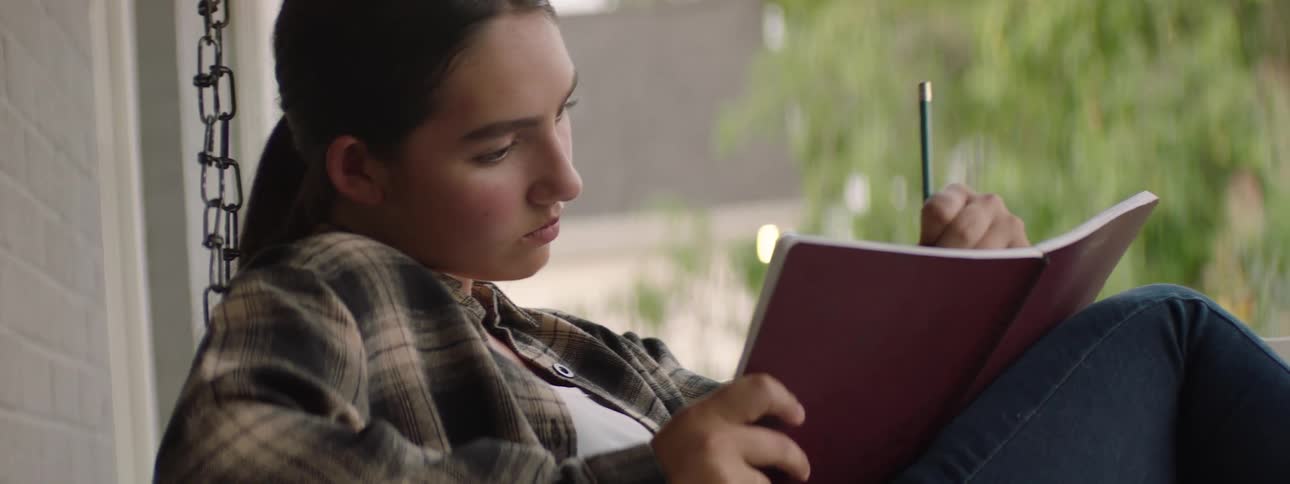 A girl is sketching in her notebook on the porch