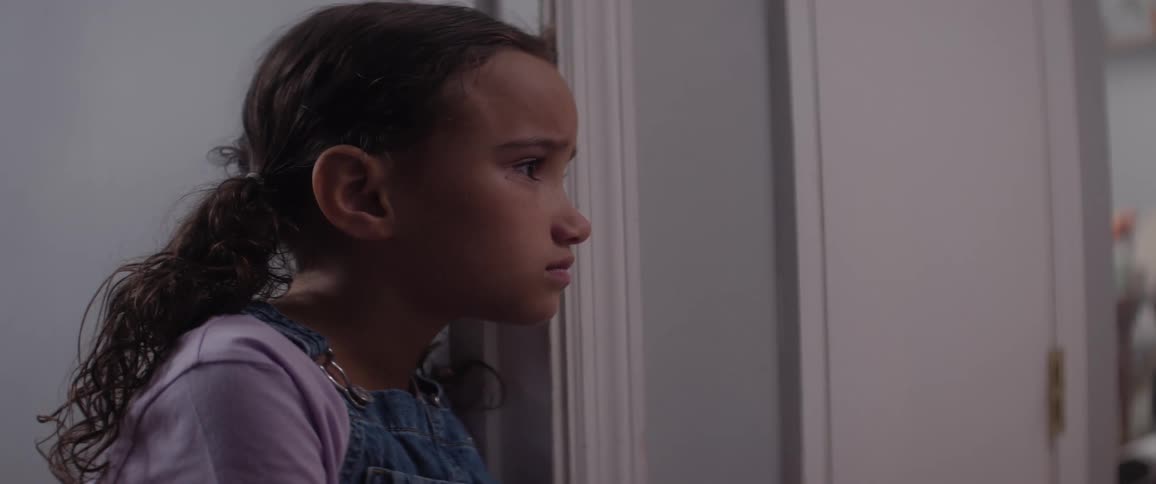 A little girl sits in a room with an anxious and worried look on her face