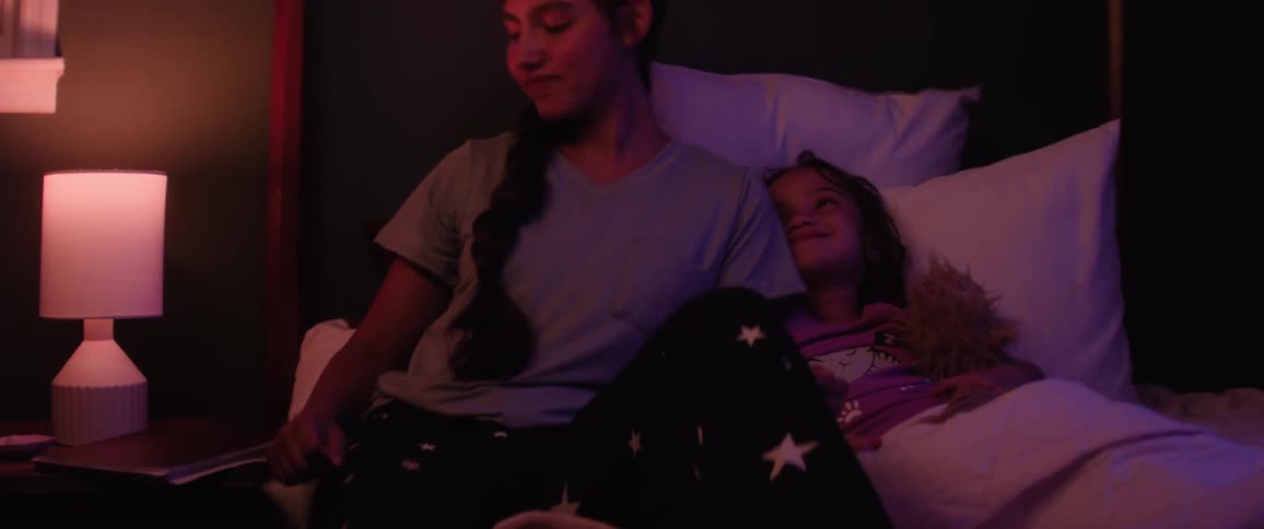 A mother sits on the bed and reads to her daughter