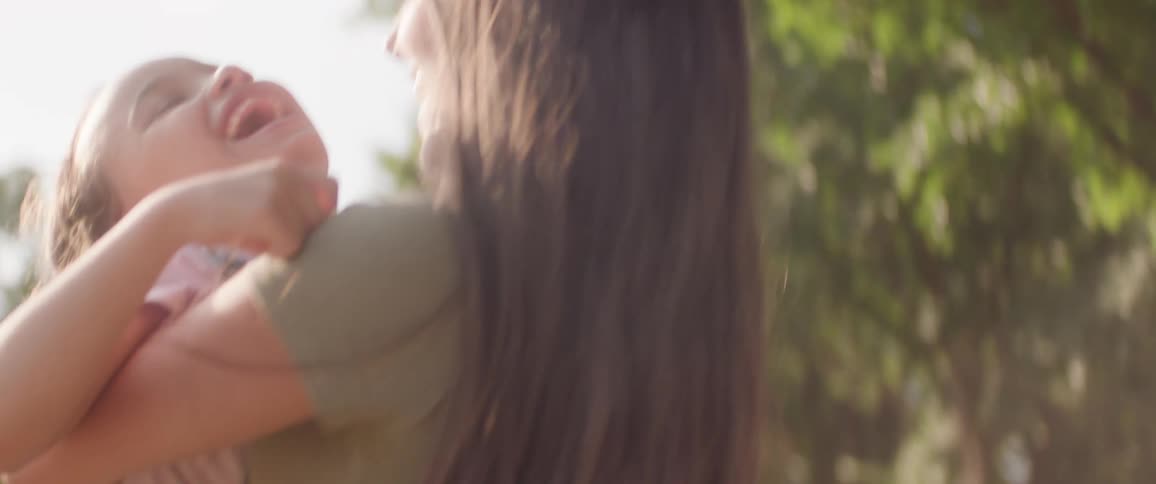 Mother hugs her daughter as they both smile and turn around under the sun