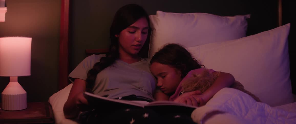 Mother is reading a story to her sleeping daughter in bed