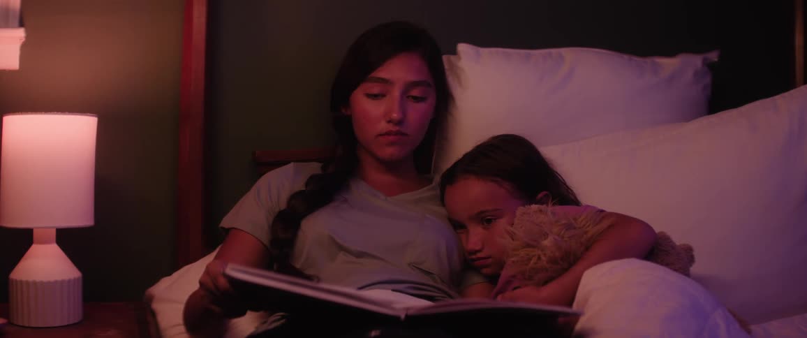 Teenage girl reads a book to her younger sister in bed at night before bedtime