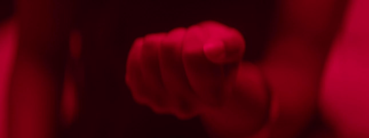 Close up of a woman clenching her fist lightly around a paper currency in her palm while seating in a red lit room