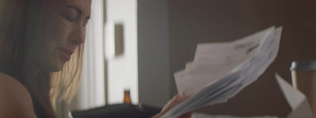 A woman reads through a series of documents indoors growing somber and sad with tears in her eyes