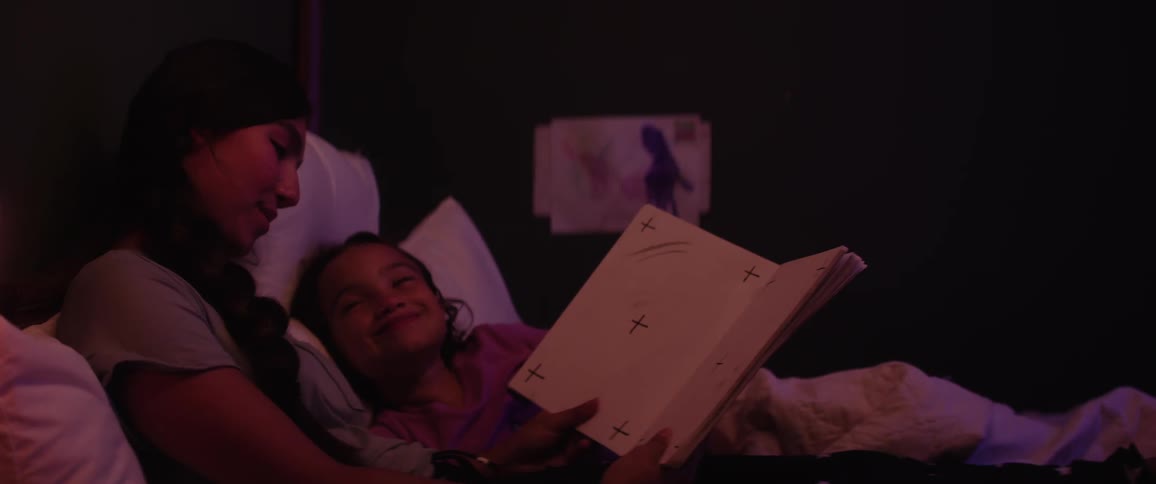 A young woman reads a bedtime story to a child as they both lie on the bed smiling after the session at night inside the bedroom