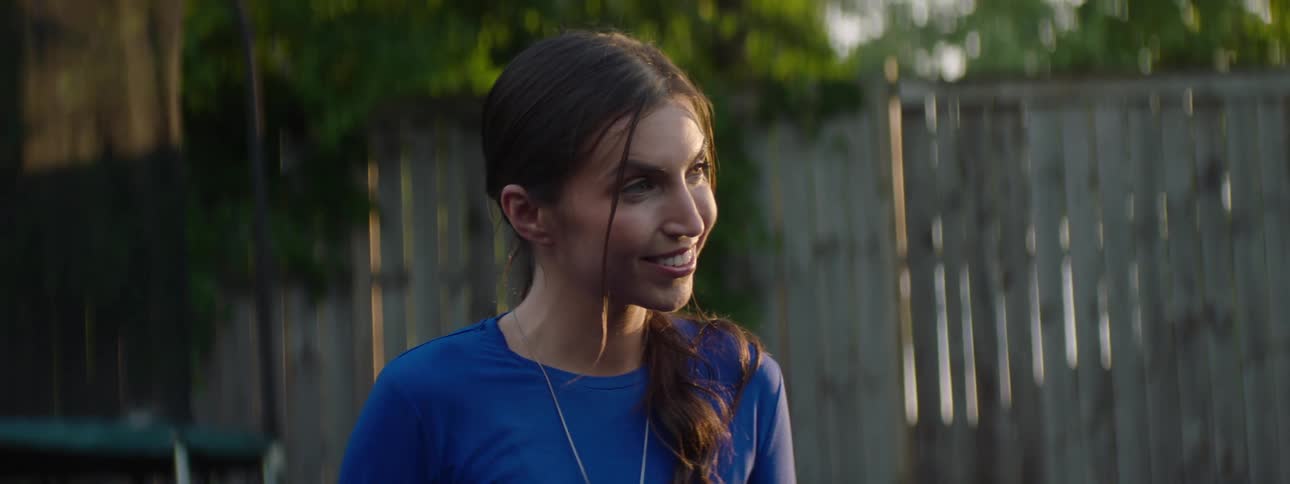 The face of a young woman who is smiling while talking and she is in an outdoor environment wearing a blue shirt