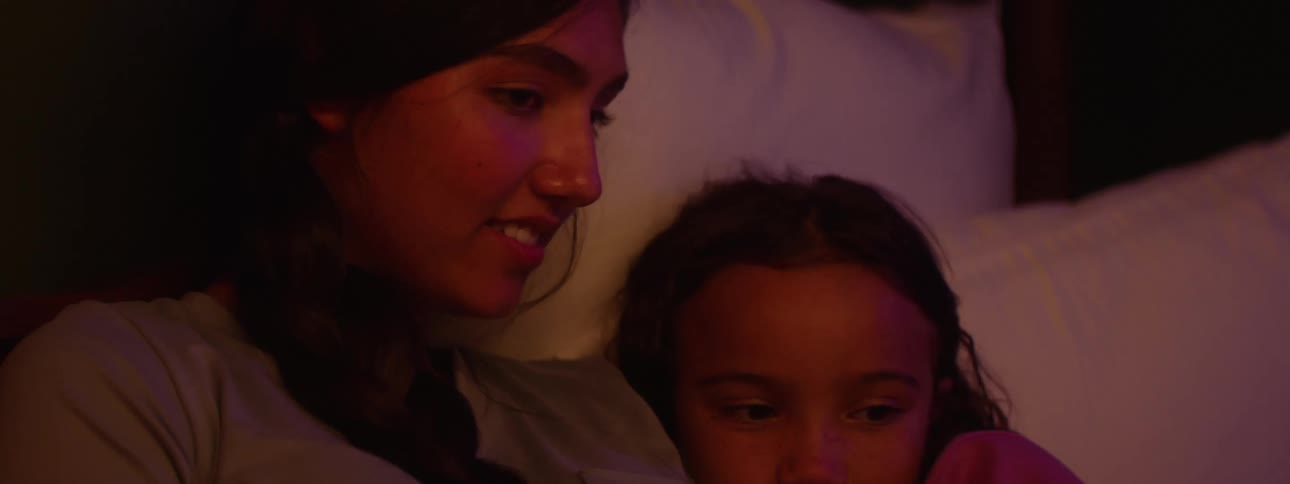 Mother reads daughter a story as they lay in bed together