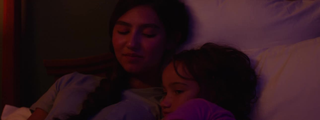 Close up of a female teenager reading a book to her younger sister on the bed at night before bedtime