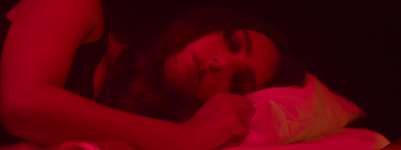 A person is shown sleeping soundly on a pillow bathed in a soft red light that gives the scene a warm intimate and slightly mysterious ambiance the closeup focuses on their face highlighting their peaceful slumber